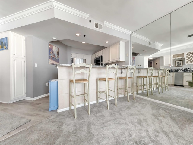 kitchen featuring stainless steel appliances, kitchen peninsula, ornamental molding, a kitchen bar, and white cabinetry