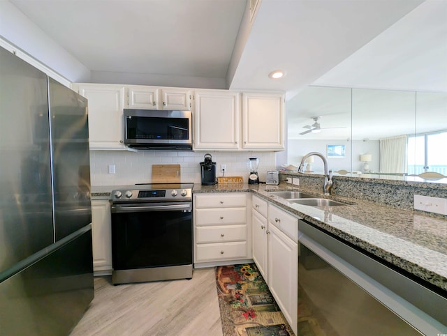 kitchen featuring white cabinets, sink, backsplash, appliances with stainless steel finishes, and light wood-type flooring