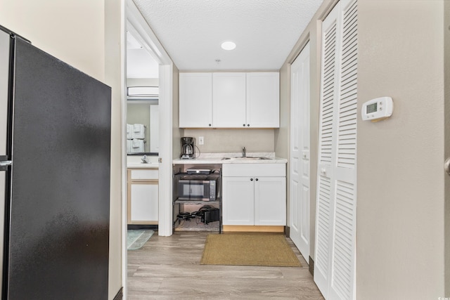 kitchen featuring light hardwood / wood-style flooring, white cabinets, a textured ceiling, and black refrigerator