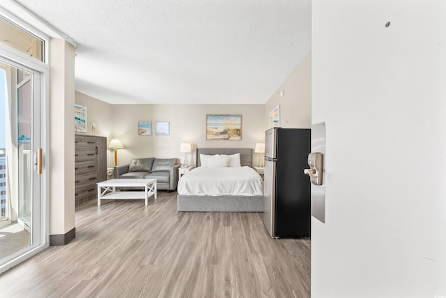 bedroom featuring access to exterior, light hardwood / wood-style flooring, multiple windows, and stainless steel refrigerator