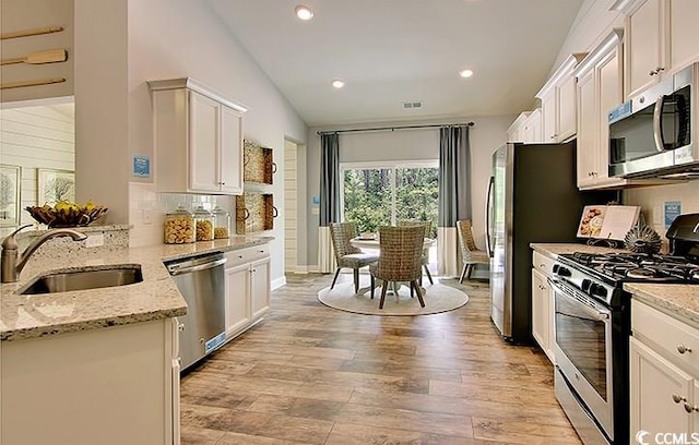 kitchen featuring a sink, lofted ceiling, light wood finished floors, white cabinets, and appliances with stainless steel finishes