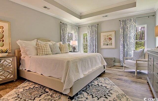 bedroom with crown molding, hardwood / wood-style flooring, and a raised ceiling