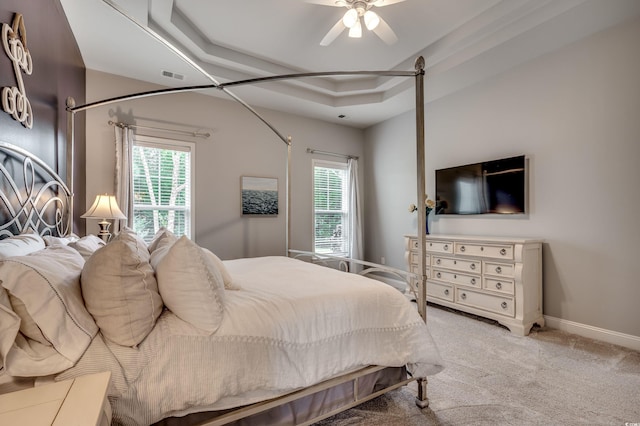 bedroom featuring a raised ceiling, carpet, multiple windows, and ceiling fan