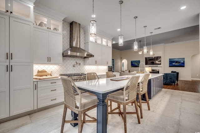 kitchen with a kitchen island, wall chimney range hood, white cabinets, and a breakfast bar