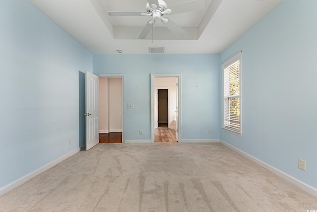 unfurnished bedroom with a raised ceiling, light colored carpet, and ceiling fan