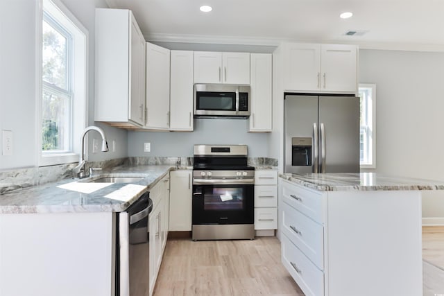 kitchen with light stone countertops, appliances with stainless steel finishes, sink, light wood-type flooring, and white cabinetry