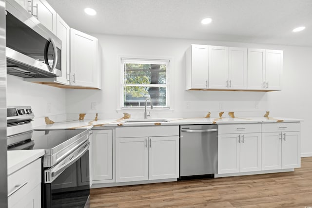 kitchen with appliances with stainless steel finishes, light hardwood / wood-style flooring, white cabinetry, and sink