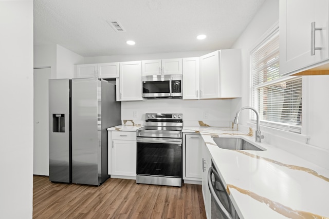 kitchen featuring sink, white cabinets, light wood-type flooring, appliances with stainless steel finishes, and a textured ceiling