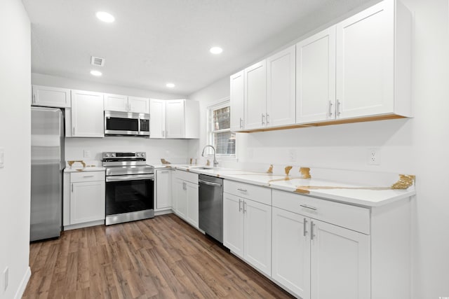 kitchen with white cabinets, dark hardwood / wood-style flooring, appliances with stainless steel finishes, light stone countertops, and sink