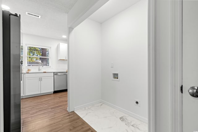 laundry area with hookup for a washing machine, hookup for an electric dryer, sink, light wood-type flooring, and a textured ceiling