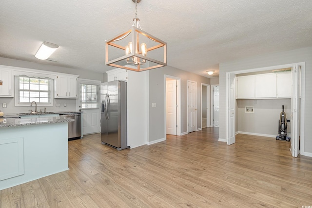 kitchen with white cabinetry, sink, hanging light fixtures, stainless steel appliances, and a textured ceiling