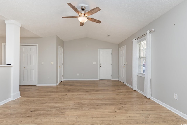 spare room with light hardwood / wood-style flooring, ceiling fan, a textured ceiling, vaulted ceiling, and ornate columns