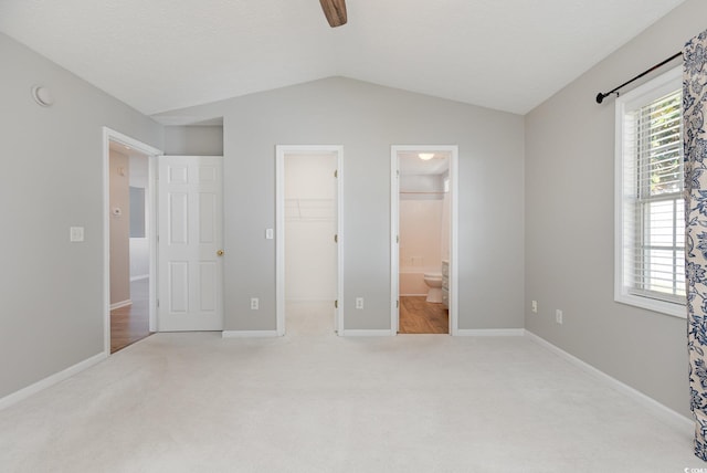 unfurnished bedroom with connected bathroom, a walk in closet, light carpet, a closet, and ceiling fan