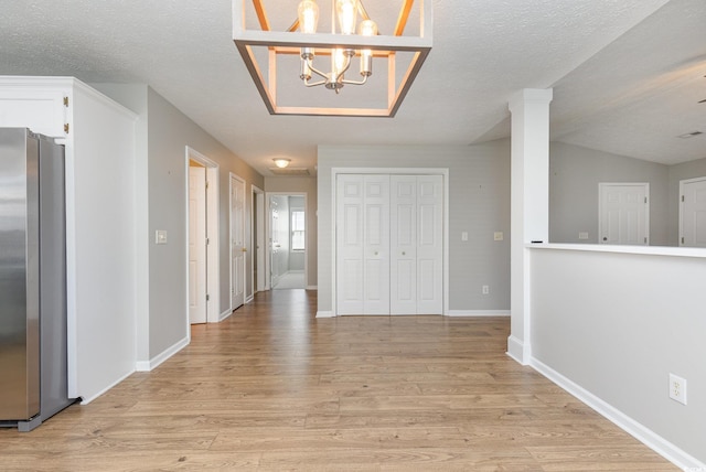 hall featuring an inviting chandelier, a textured ceiling, and light wood-type flooring