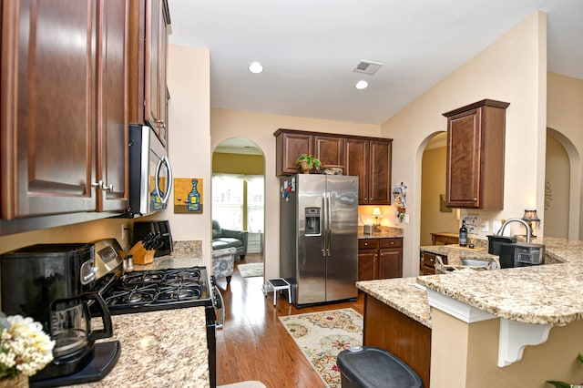 kitchen featuring light stone counters, kitchen peninsula, light hardwood / wood-style flooring, appliances with stainless steel finishes, and a breakfast bar area