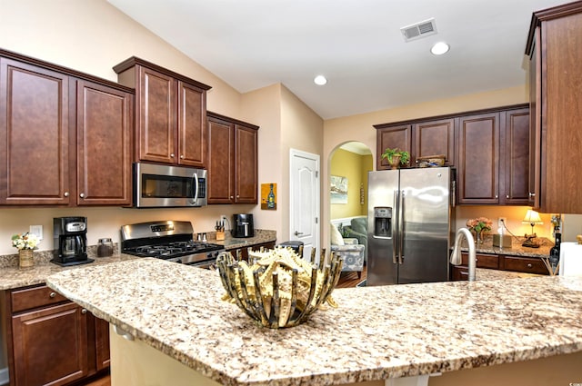 kitchen with appliances with stainless steel finishes, lofted ceiling, light stone counters, and dark brown cabinets