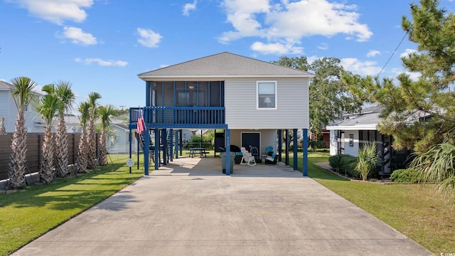 view of front of property with a front yard, a sunroom, a carport, fence, and concrete driveway