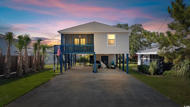 coastal home with a front yard, a shingled roof, a carport, fence, and driveway