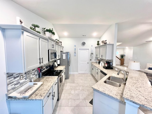 kitchen featuring decorative backsplash, sink, light stone countertops, vaulted ceiling, and appliances with stainless steel finishes