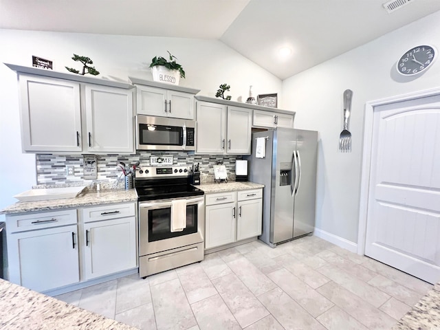 kitchen with lofted ceiling, appliances with stainless steel finishes, light stone counters, and tasteful backsplash