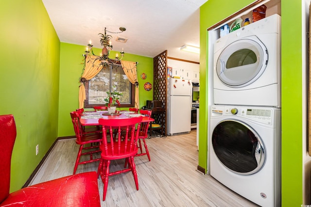 laundry area with stacked washing maching and dryer, light hardwood / wood-style flooring, and an inviting chandelier