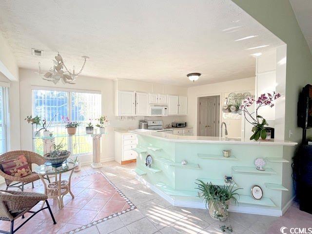 kitchen with white cabinets, a textured ceiling, white appliances, and light tile patterned flooring