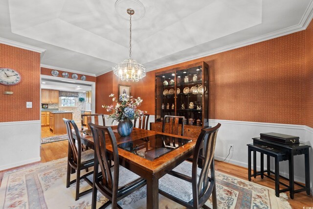 dining room with an inviting chandelier, ornamental molding, a raised ceiling, and light wood-type flooring