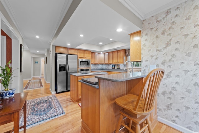 kitchen with ornamental molding, appliances with stainless steel finishes, a kitchen bar, and kitchen peninsula