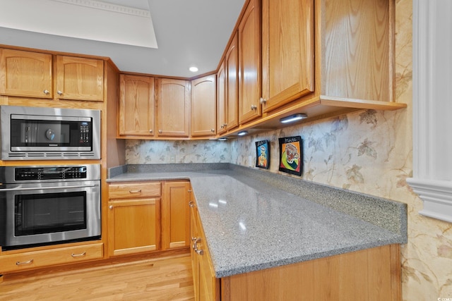 kitchen featuring stainless steel appliances, light stone countertops, decorative backsplash, and light wood-type flooring