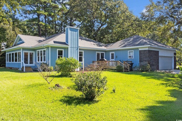 rear view of property with a garage, a wooden deck, a sunroom, and a yard