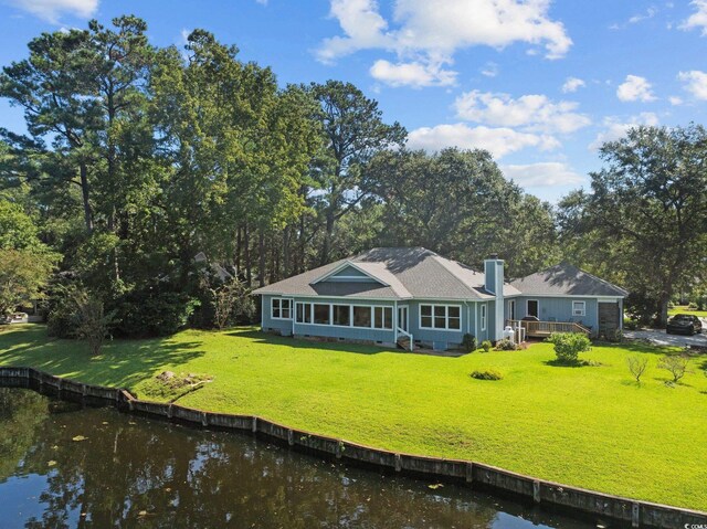 rear view of house featuring a deck with water view, a lawn, and a sunroom