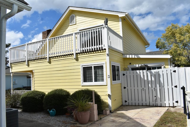 view of home's exterior featuring central AC unit, a chimney, fence, a balcony, and a gate