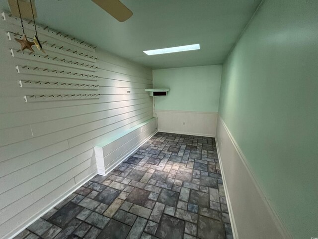unfurnished room featuring brick floor, wooden walls, and baseboards