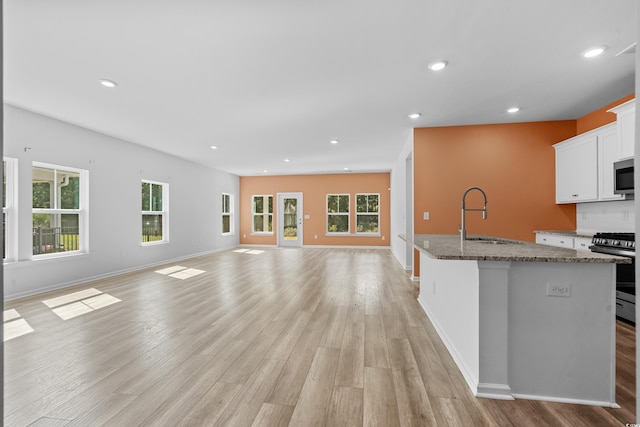 kitchen featuring appliances with stainless steel finishes, sink, stone counters, white cabinetry, and an island with sink