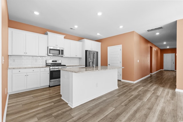 kitchen featuring a center island with sink, light stone counters, white cabinetry, and appliances with stainless steel finishes