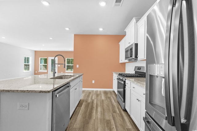 kitchen with light stone countertops, sink, stainless steel appliances, an island with sink, and white cabinets