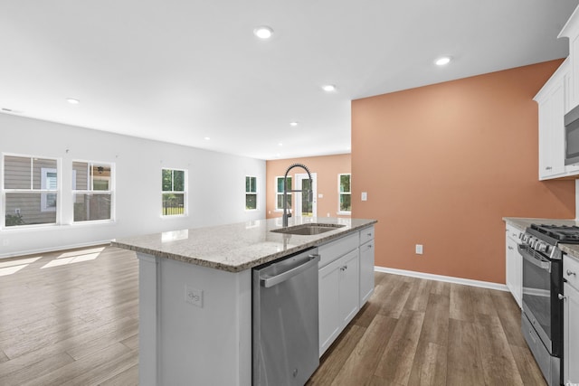 kitchen with stainless steel appliances, sink, white cabinets, light hardwood / wood-style floors, and an island with sink