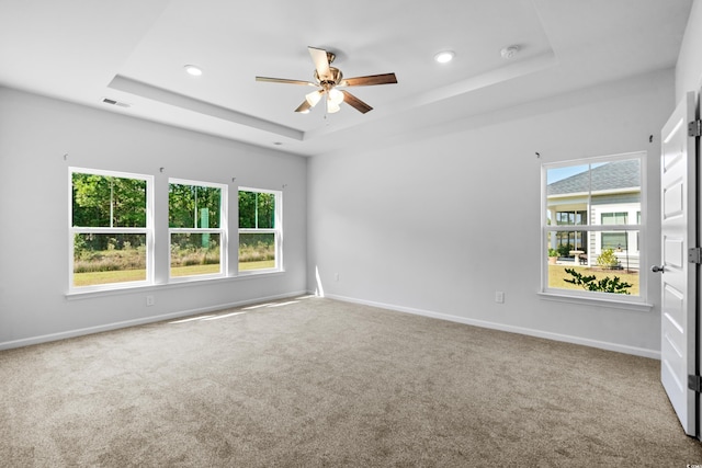 carpeted empty room with ceiling fan, a raised ceiling, and a wealth of natural light