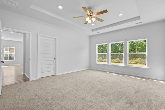 carpeted spare room with a raised ceiling and ceiling fan