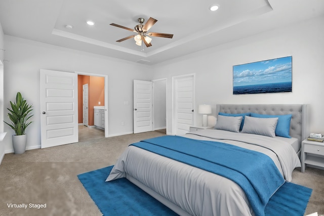 bedroom with ceiling fan, a raised ceiling, carpet floors, and connected bathroom