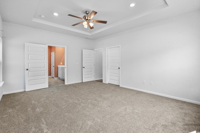 unfurnished bedroom with carpet, ceiling fan, connected bathroom, and a tray ceiling