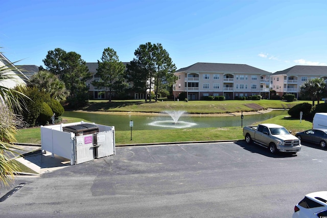 view of car parking featuring a lawn and a water view