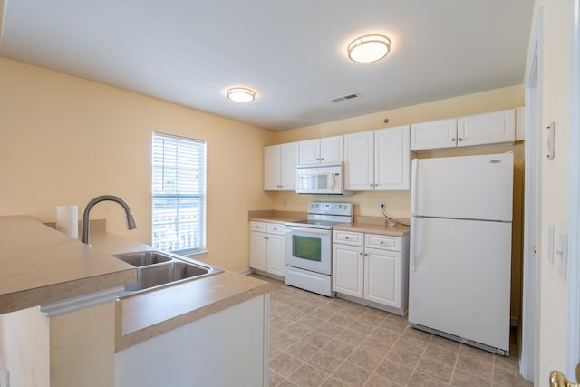 kitchen with white appliances, a sink, visible vents, and white cabinets