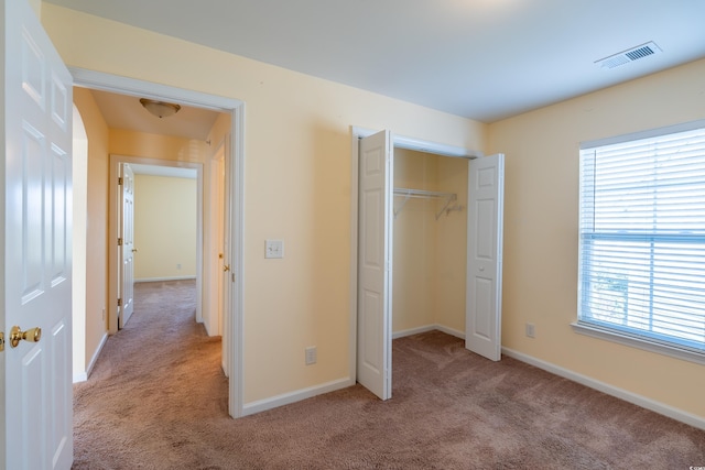 unfurnished bedroom with a closet, visible vents, light carpet, and baseboards