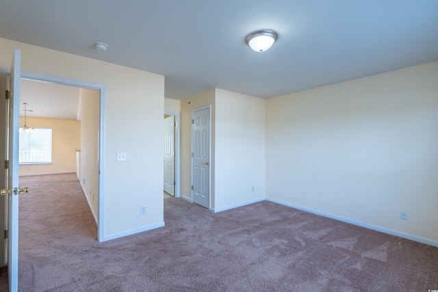 carpeted empty room with baseboards and a chandelier