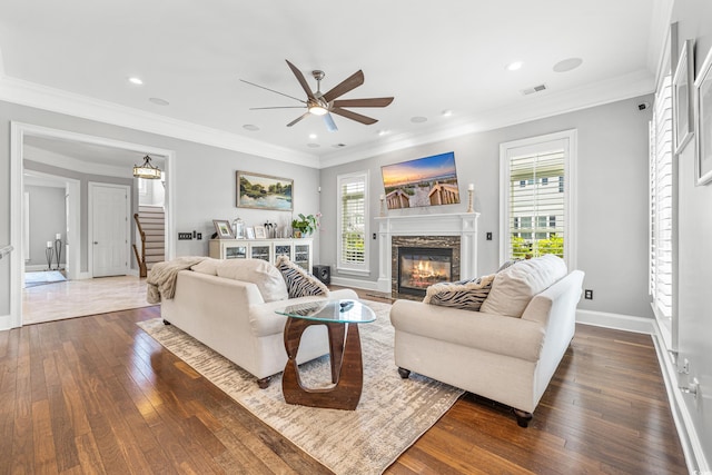 living room featuring ornamental molding, a stone fireplace, dark hardwood / wood-style floors, and ceiling fan