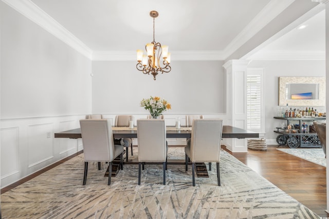 dining space featuring dark wood-type flooring, ornate columns, ornamental molding, and a chandelier