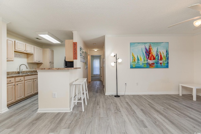 kitchen featuring sink, light hardwood / wood-style flooring, a textured ceiling, a breakfast bar, and ornamental molding