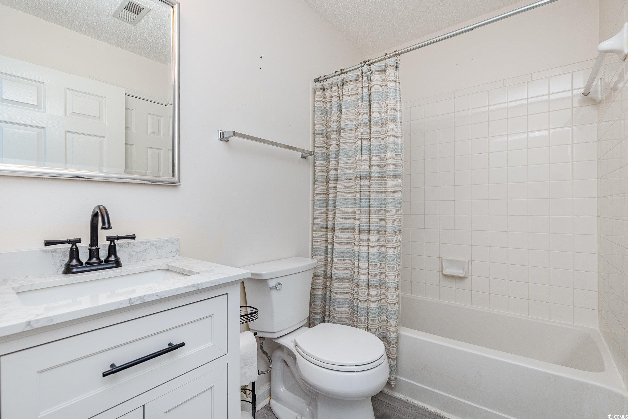 full bathroom with vanity, toilet, a textured ceiling, and shower / tub combo