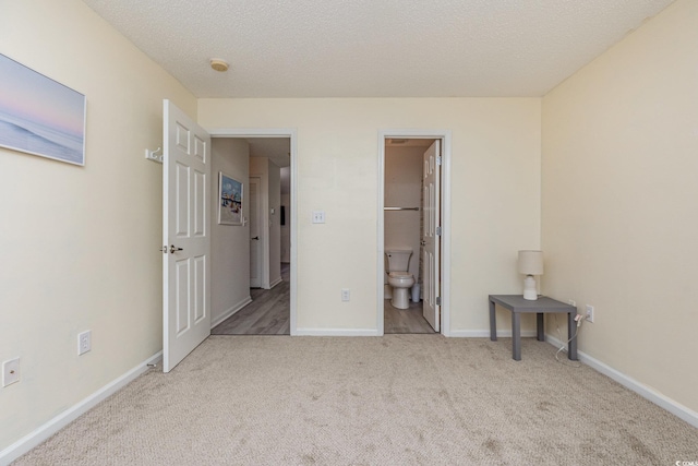 unfurnished bedroom featuring ensuite bathroom, light colored carpet, and a textured ceiling